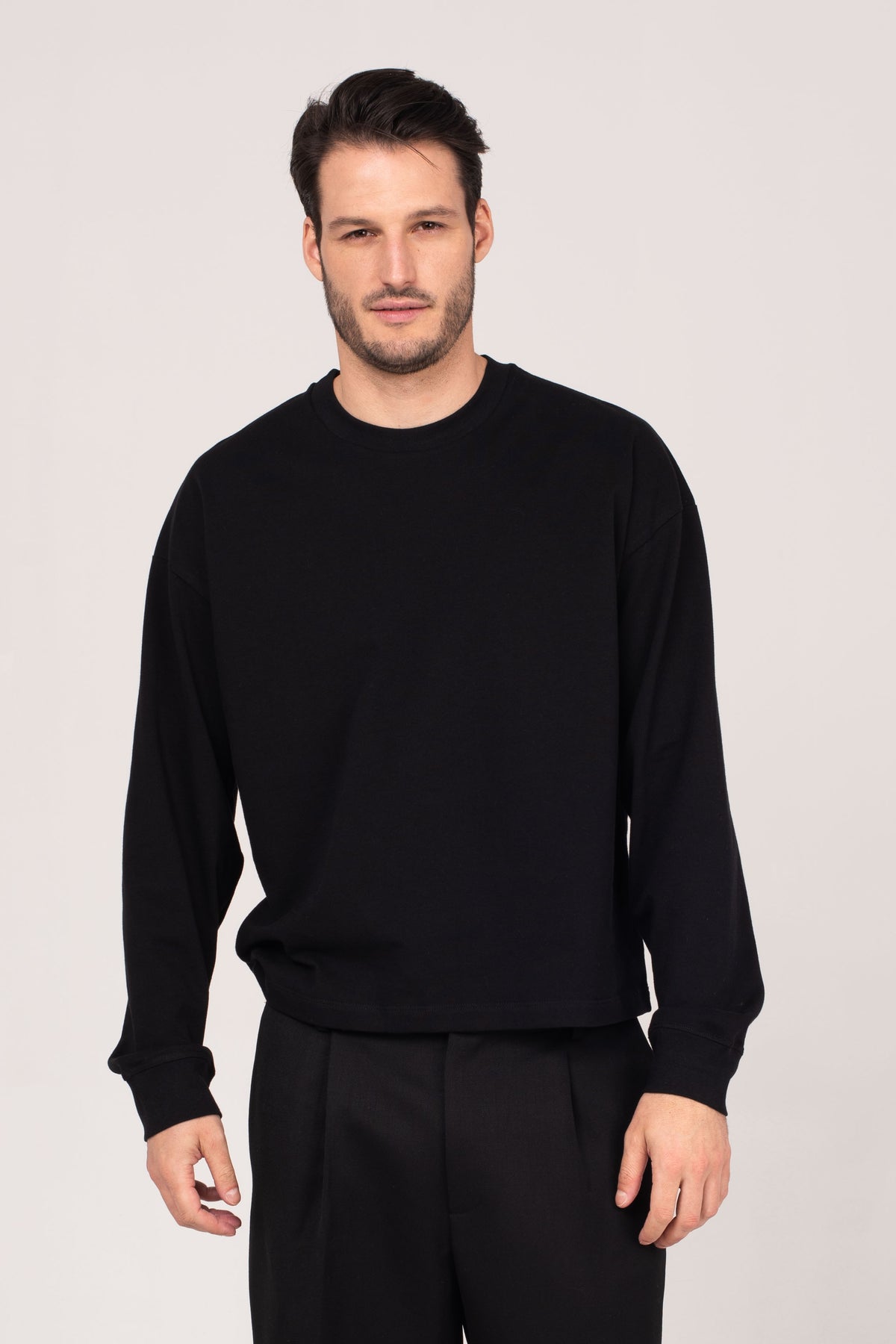 A male model wearing the NO.29 black long sleeve shirt, styled with pleated trousers. A minimalist, timeless wardrobe essential made in NYC, inspired by European tailoring.