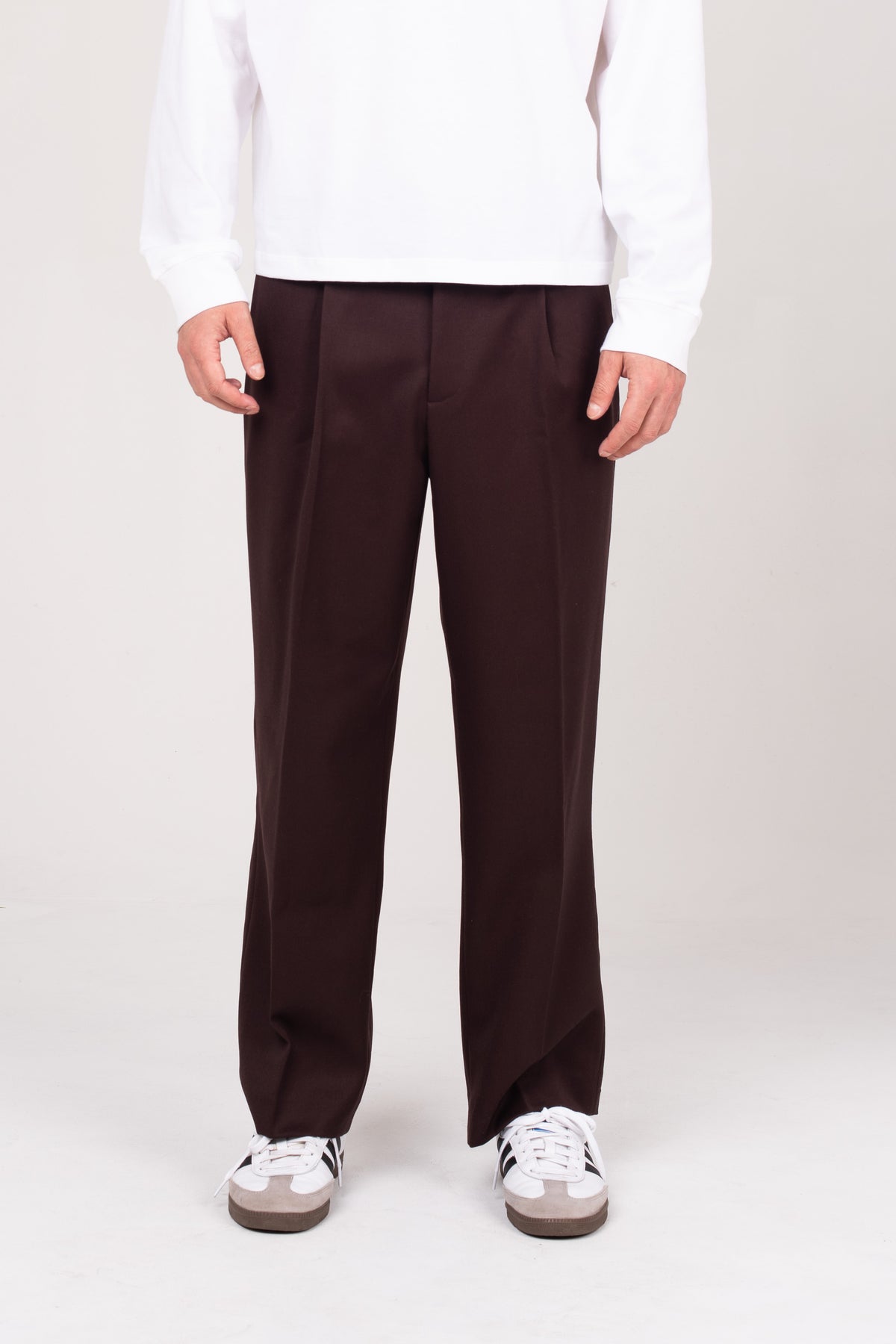 A close-up of the NO.29 brown pleated trousers, styled with a white NO.29 long sleeve shirt and sneakers. A modern take on classic tailoring, designed for effortless wear and versatility.