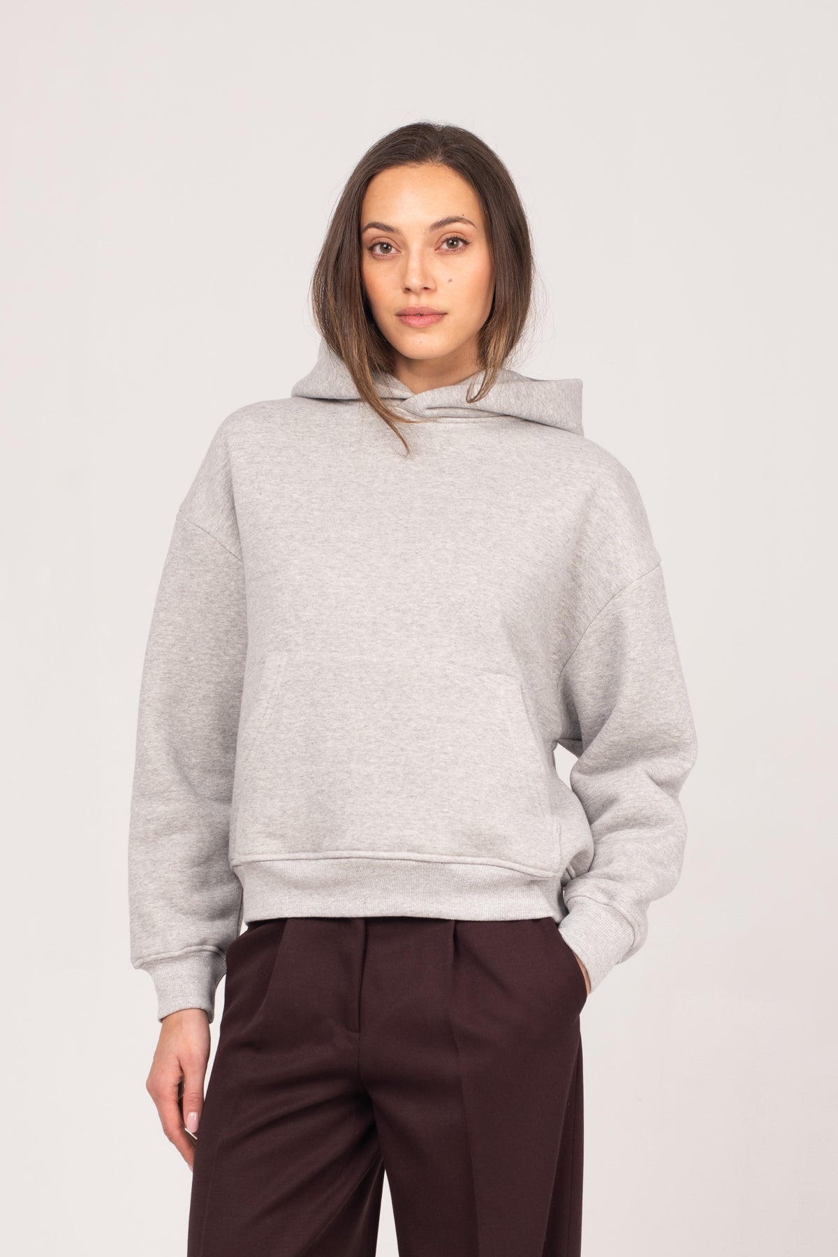 A close-up of the NO.29 women's grey heavyweight hoodie, styled with brown NO.29 pleated trousers. A relaxed yet refined essential, designed for elevated comfort and effortless everyday wear.